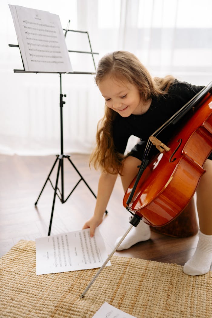 Smiling child practicing cello at home with sheet music and music stand.